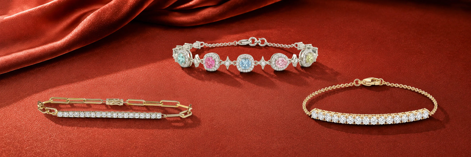 Lab-grown diamond chain bracelets in yellow gold — pavé bar paperclip link bracelet, multi-color fancy cushion cut station bracelet with blue pink and yellow diamonds, and curved round brilliant bar bracelet on red satin