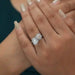 [a woman's hand holding a diamond engagement ring]-[Ouros Jewels]