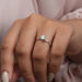 [a woman's hand holding a round diamond engagement ring]-[Ouros Jewels]