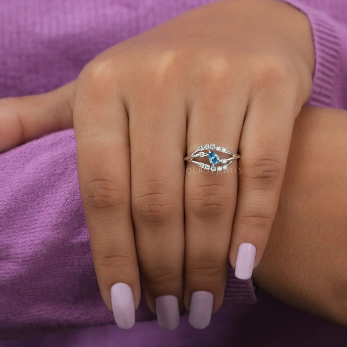 In finger front view of bypass set blue pear shaped engagement ring crafted with 14k white gold.