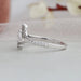 Round accent stones studded on the curved shank of pear shaped dainty engagement ring