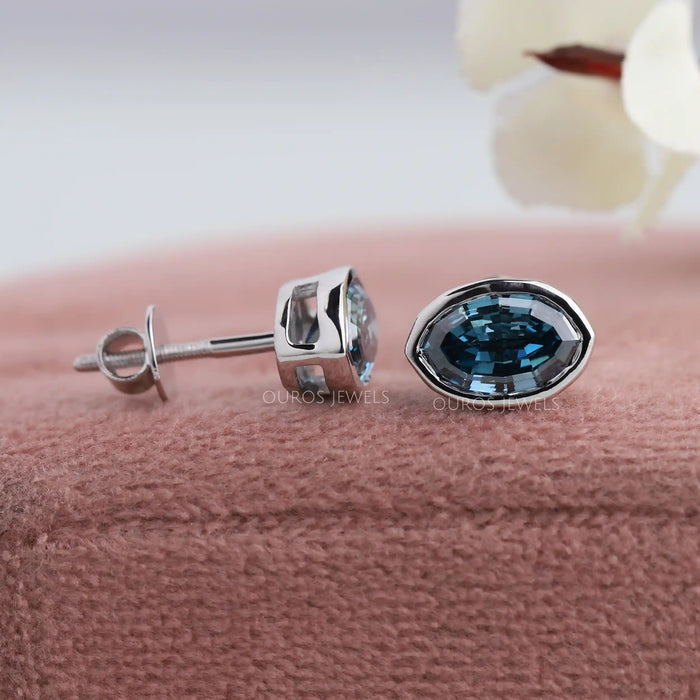 Side view of oval blue stud earrings set in bezel, crafted with 14k white gold.