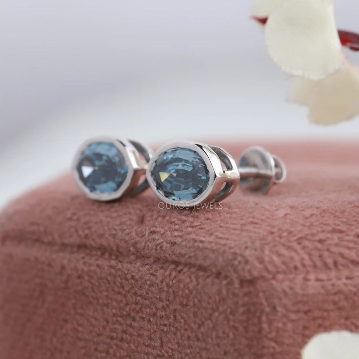 Side view of step cut blue oval diamond stud earrings set in bezel.