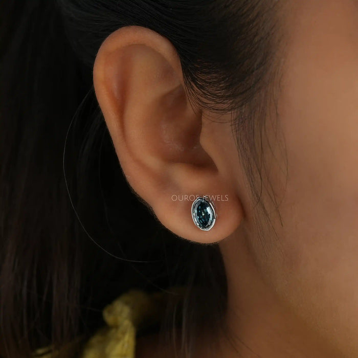In ear front view of bezel set earrings step cut blue oval diamond earrings.