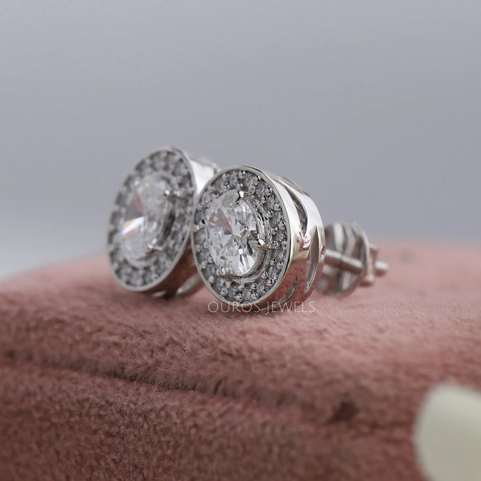 The single center oval cut diamonds are surrounded by a halo of round diamonds in screw back setting